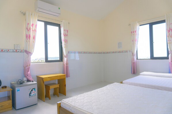 Une chambre avec deux lits, un petit bureau, un réfrigérateur et des fenêtres avec des rideaux.