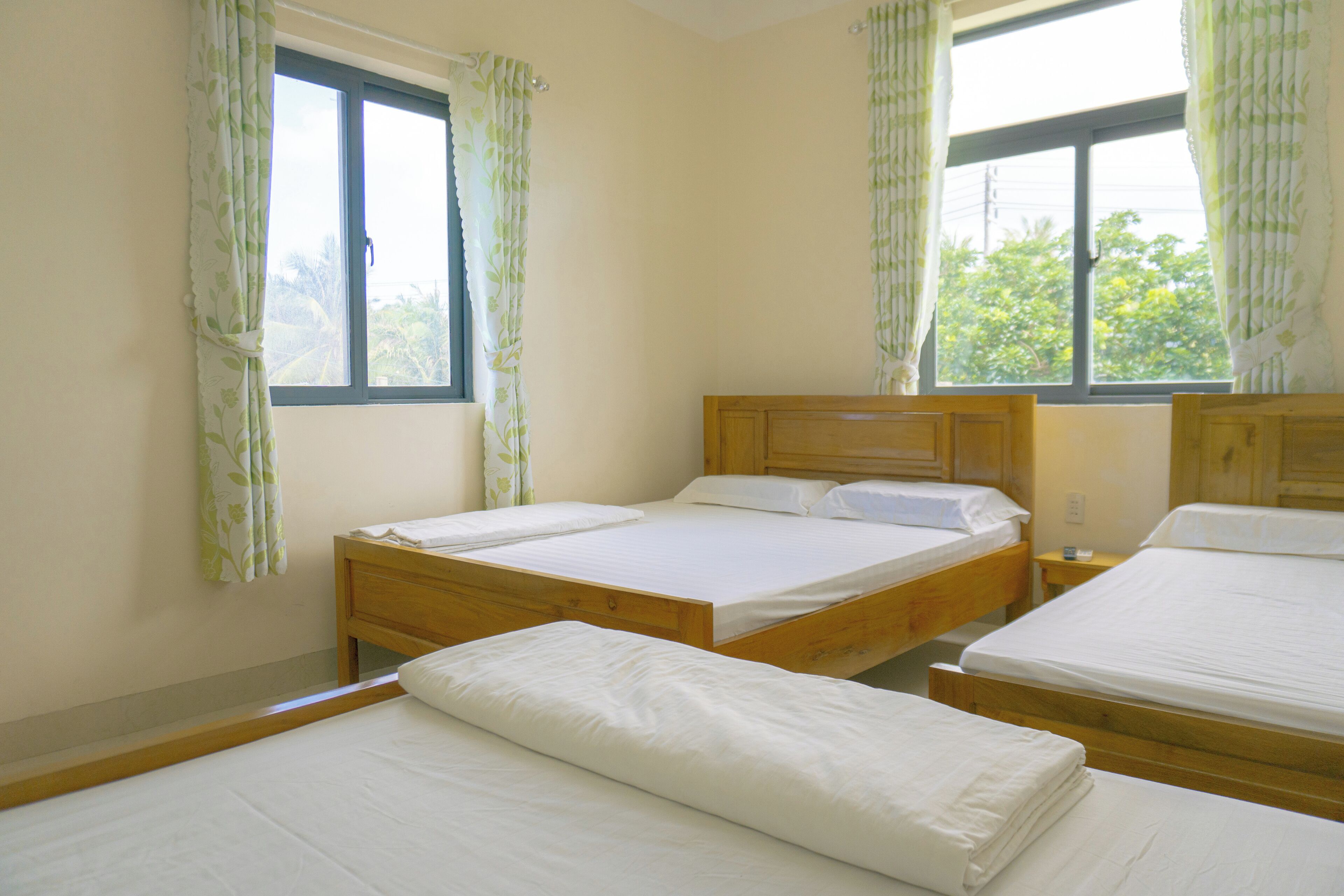 Une chambre avec deux lits en bois, une tête de lit en bois et une fenêtre avec des rideaux.