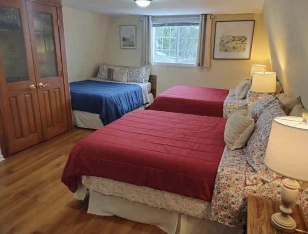 A bedroom with two beds, wooden flooring, a wardrobe, and a window with curtains.