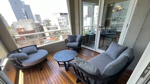 Un balcon avec un plancher en bois, des canapés gris et une table ronde.