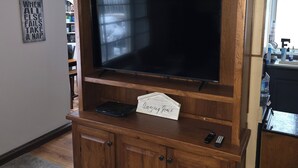Un meuble de rangement en bois abritant un téléviseur à écran plat, une petite étagère avec un panneau et une télécommande posée sur l’étagère inférieure.
