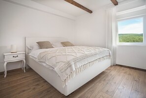 Une chambre à coucher avec un lit, une table de chevet et une fenêtre donnant sur un paysage verdoyant.