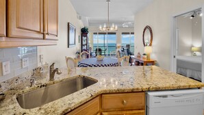 A kitchen with granite countertops, stainless steel sink, wooden cabinets, and a view to the outside.