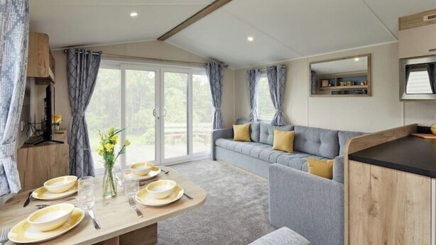 Ein modernes Wohnzimmer mit einem grauen Sofa, einem Holzessttisch mit gelben Tellern und einem großen Fenster mit Vorhängen.