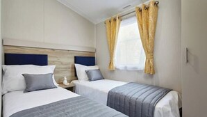 Ein Hotelzimmer mit zwei Betten, jeweils mit Kopfteil, Nachttisch und einem Fenster mit gelben Vorhängen.