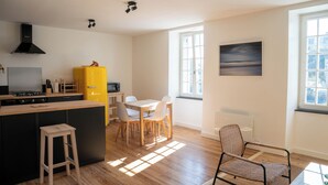 A modern kitchen with a yellow refrigerator, wooden island, and bar stools. There is a dining area with a table and chairs, and a large window providing natural light.