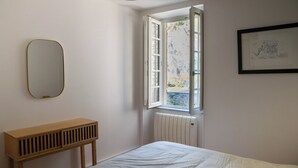 A bedroom with a bed, a bedside table, a window with a view of the outside, and a framed picture on the wall.