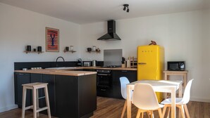 A modern kitchen with a central island, black cabinetry, a yellow refrigerator, and a dining area with white chairs.