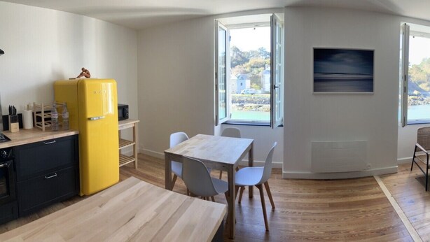 A compact living space with a kitchen, dining area, and seating area. It features a yellow refrigerator, a dining table with chairs, a green sofa, and a TV mounted on the wall.