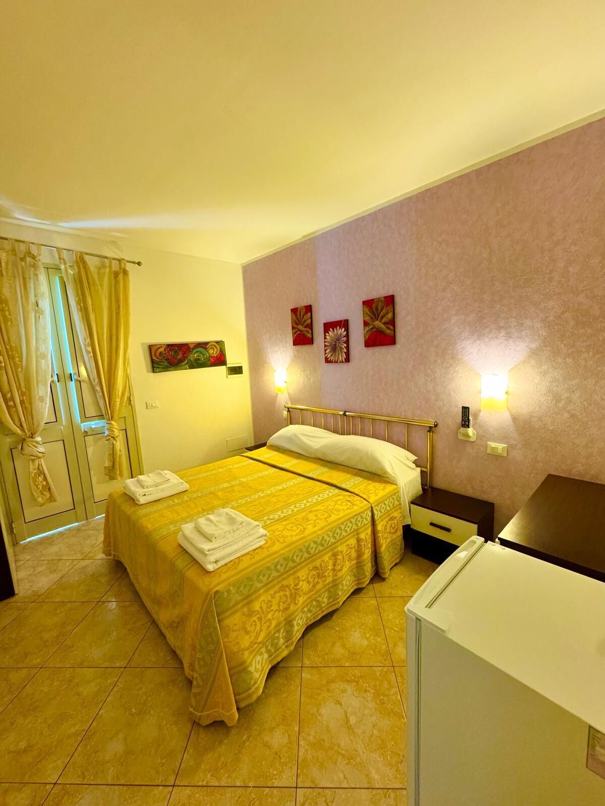 A hotel room with a double bed, a small bedside table, a nightstand, a lamp, and a wardrobe.