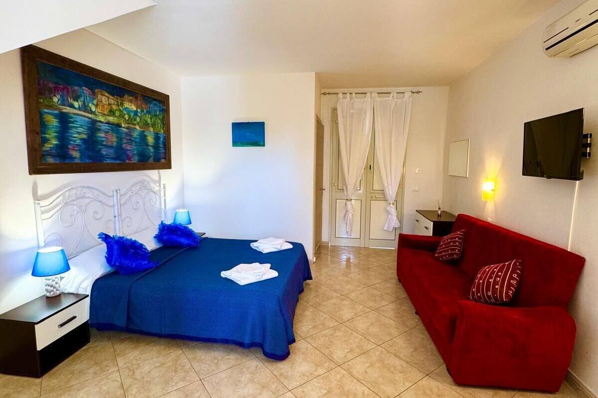 A bedroom with a bed, a red sofa, a TV, and a painting on the wall.