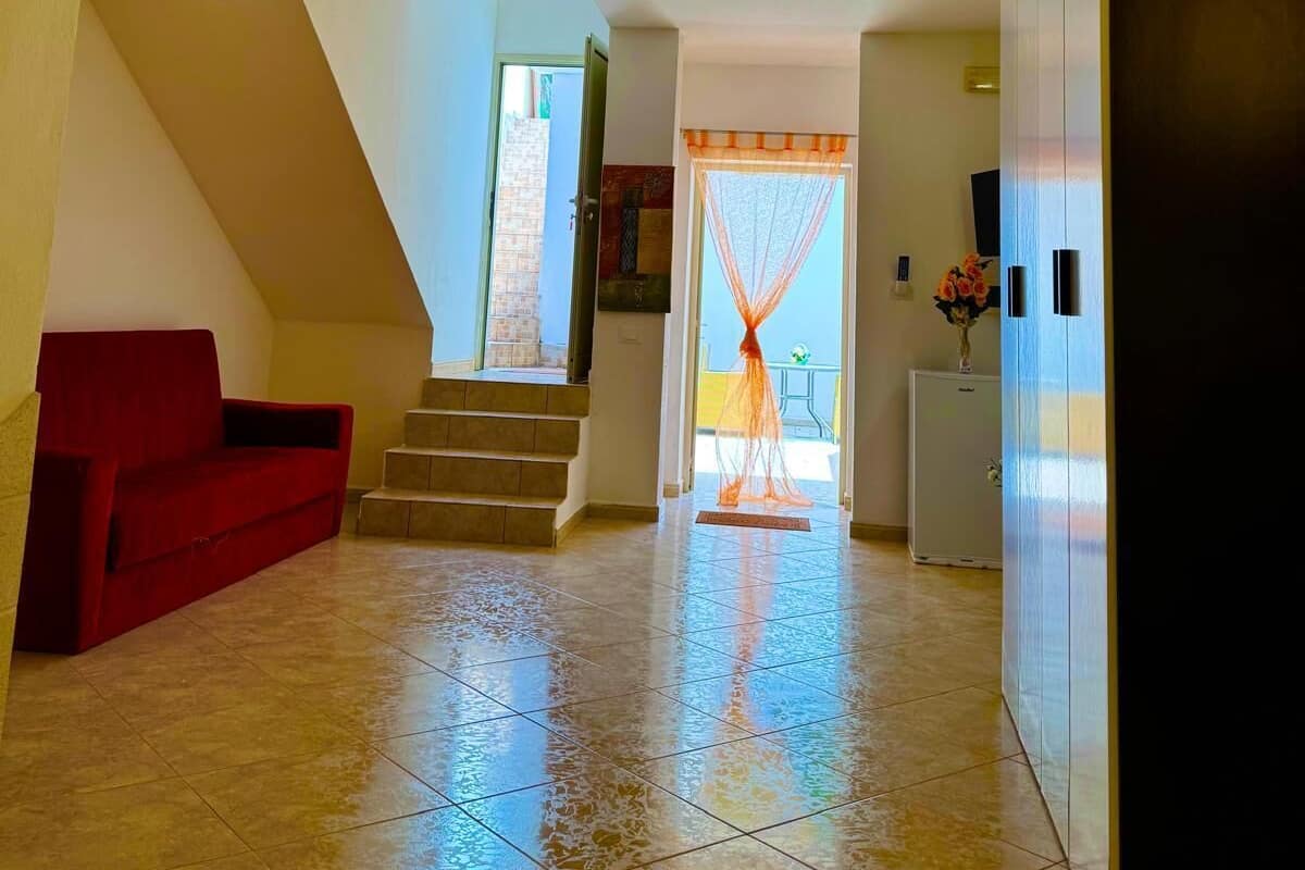 A spacious hallway with a red sofa, a staircase, and a door leading to a balcony.