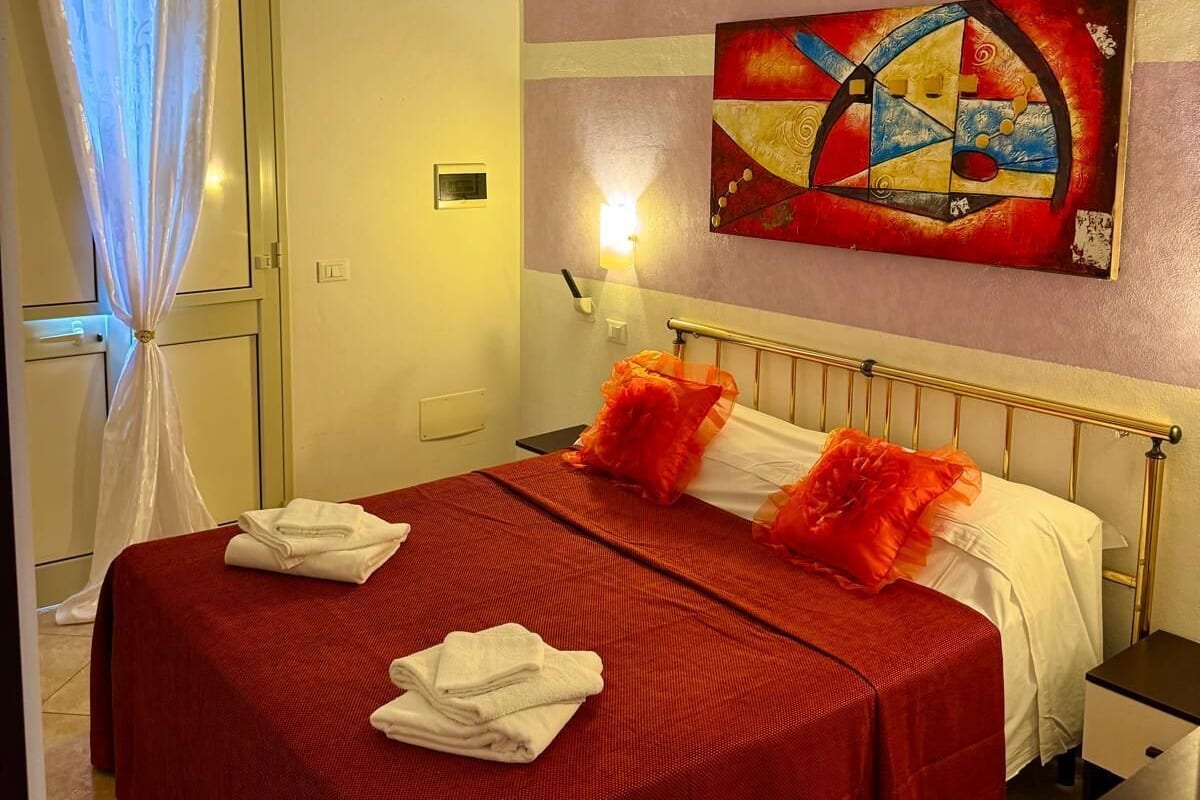 A hotel room with a bed, a painting on the wall, and a nightstand.
