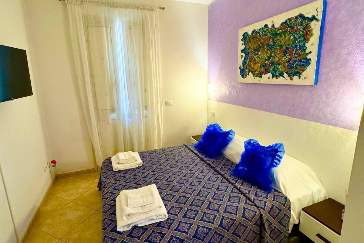 A room with a bed, a nightstand, a painting on the wall, and a window with curtains.