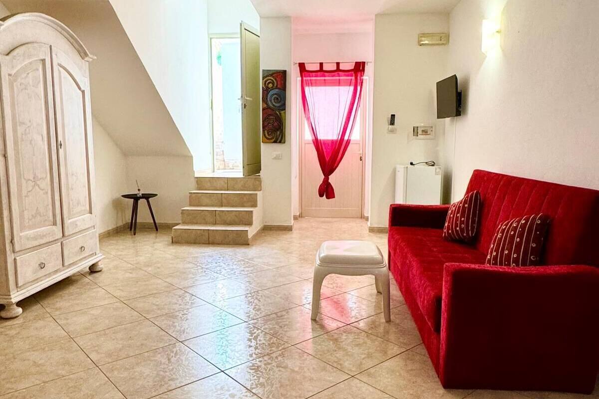 A spacious living room with a red sofa, a white cabinet, and a staircase leading to another room.