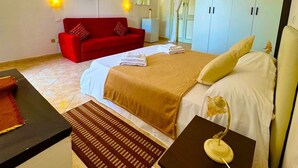 A hotel room with a bed, a red sofa, a TV, and a wardrobe. - Residence Luxora (Melendugno)