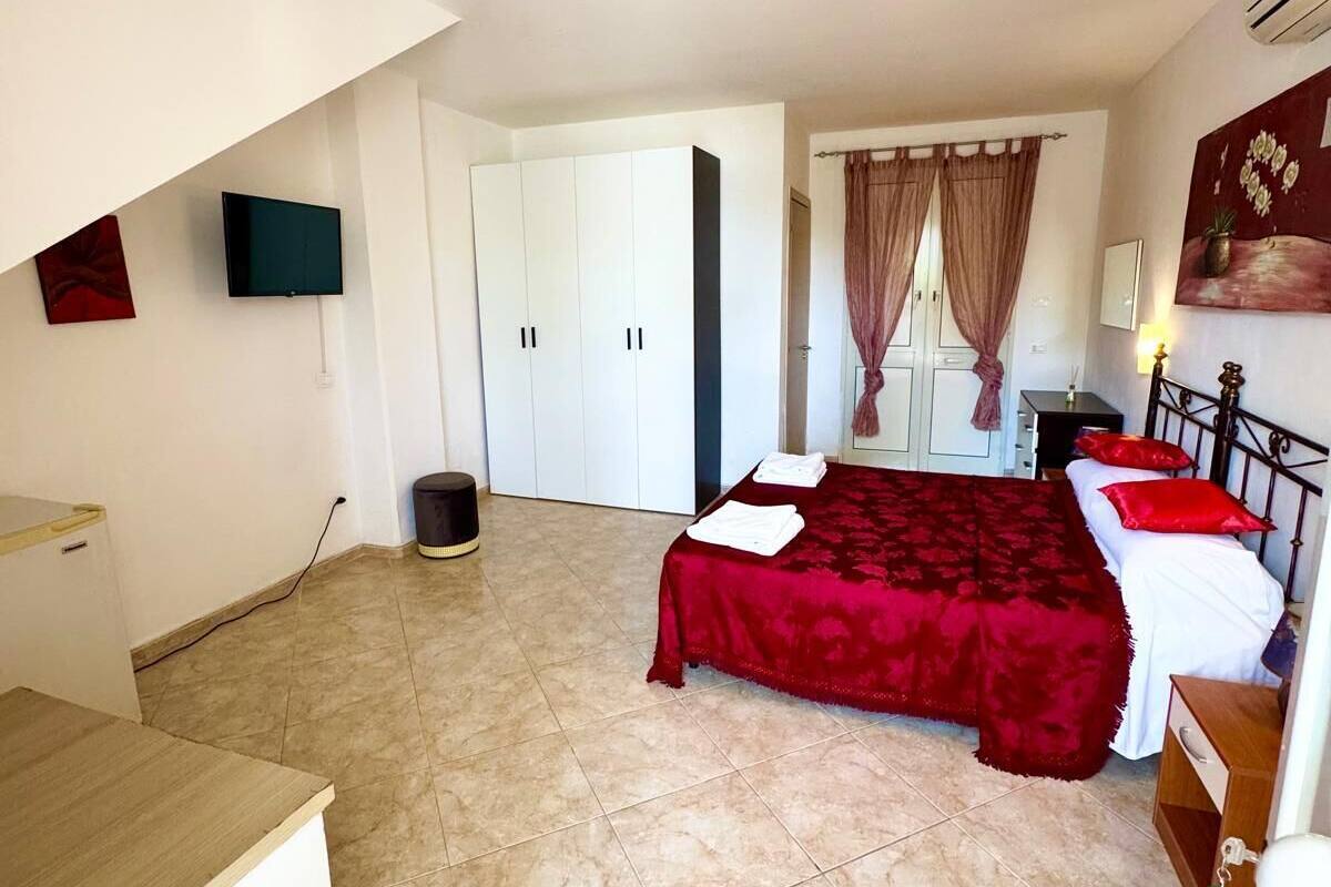 A bedroom with a bed, a desk, a chair, a TV, and a door.