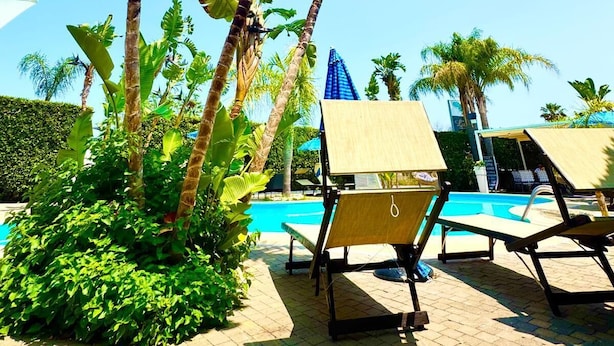 A poolside area with lounge chairs, palm trees, and a clear blue sky. - Residence Luxora (Melendugno)