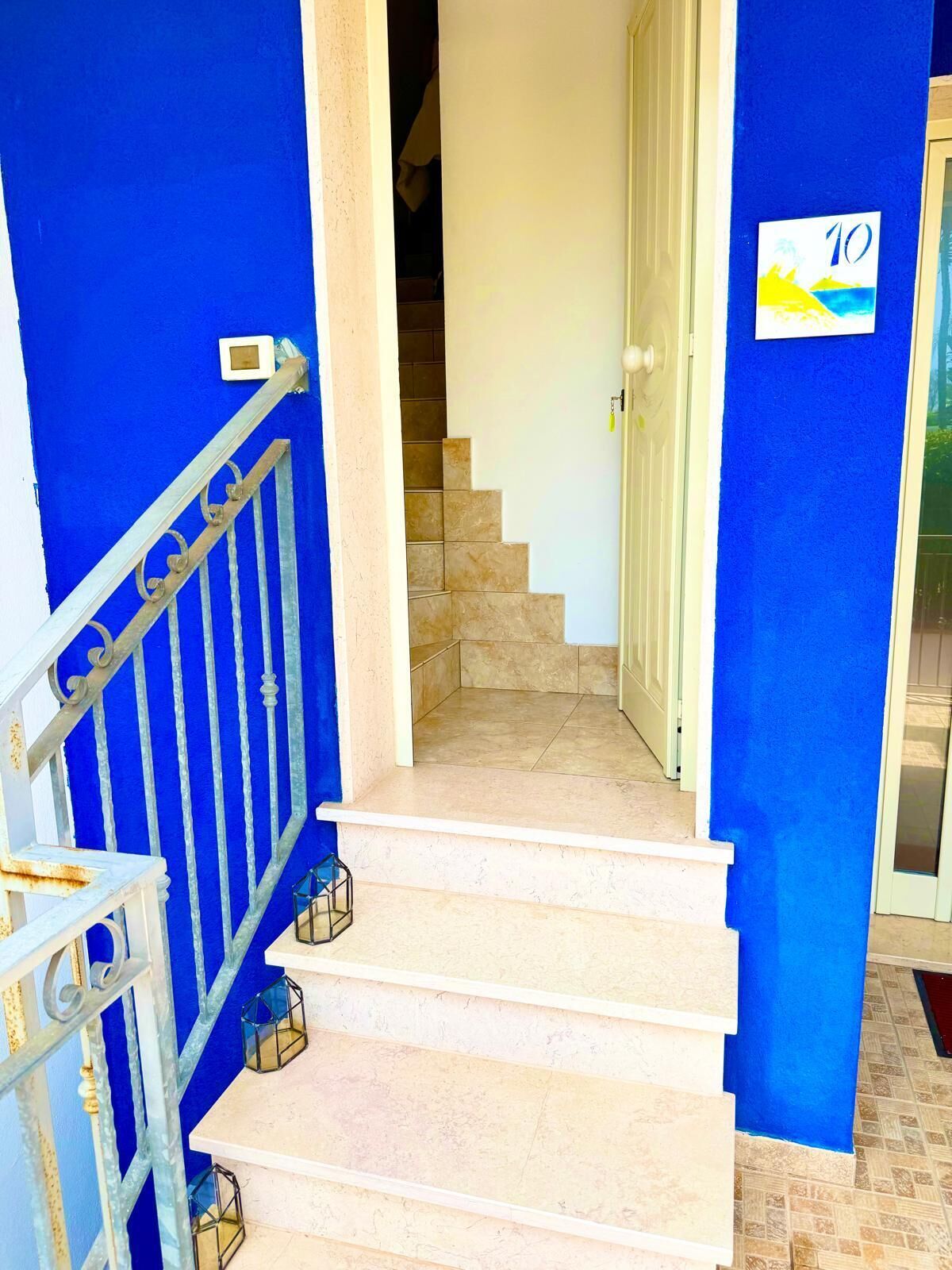 Una escalera con peldaños color beige que lleva a una plataforma, flanqueada por paredes azules y una puerta blanca.