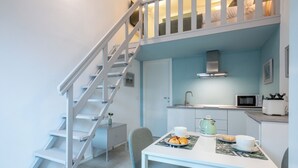 A compact kitchen with a microwave, kettle, and toaster. A dining table with chairs is positioned under a staircase.