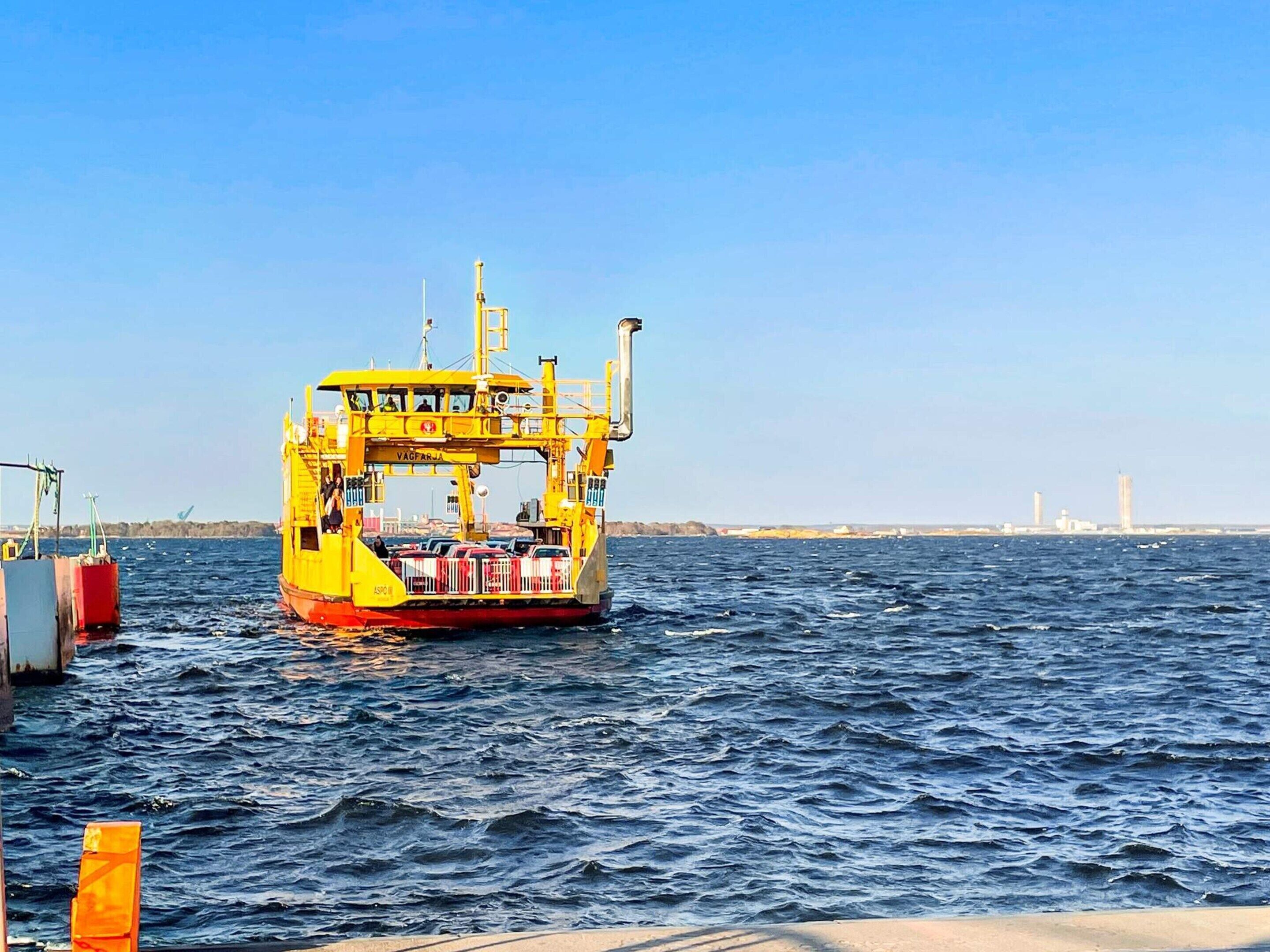 Eine gelbe Fähre liegt an einem Steg, mit freiem Blick auf das Wasser und Gebäude in der Ferne.