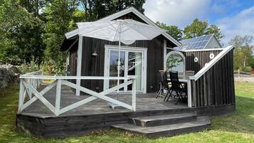 Una cabaña de madera con terraza, zona de comedor y paneles solares en el techo.