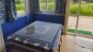 Een kamer met een blauwe bank, een tafel met een tafelkleed met patroon, en uitzicht op een groen veld door een raam.