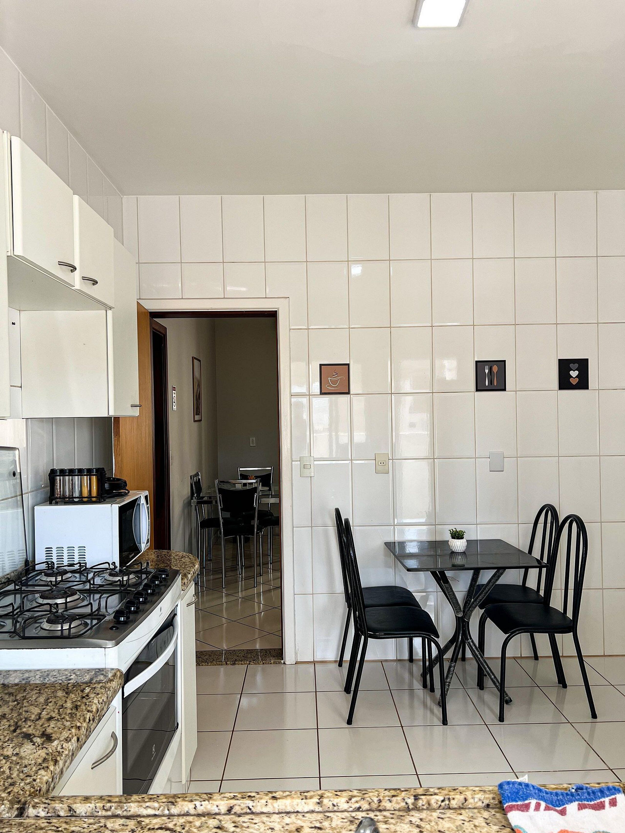A kitchen with white cabinets, a gas stove, a microwave, and a dining area with a table and chairs.