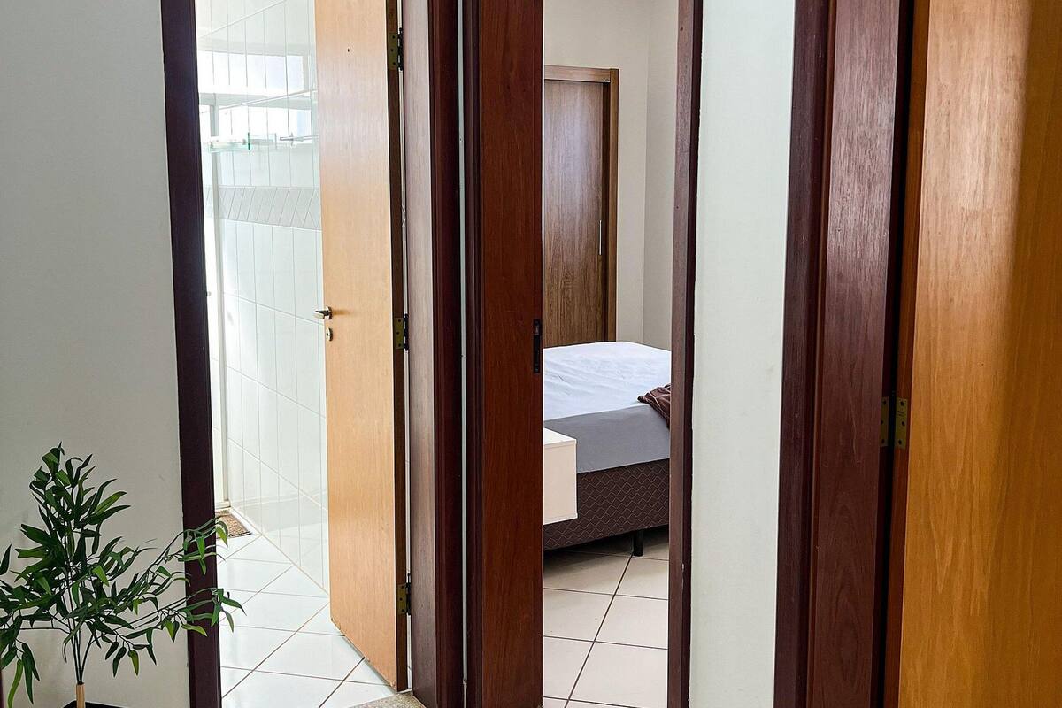 A hallway with wooden doors leading to a bedroom with a bed and a nightstand.