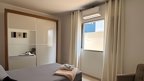 A modern bedroom with a bed, a chair, a desk, and a window with curtains.