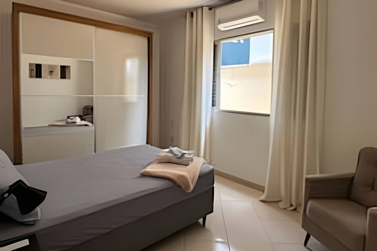 A modern bedroom with a bed, a chair, a desk, and a window with curtains.