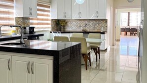 A modern kitchen with white cabinets, a black island, and a dining area with a glass table and chairs.