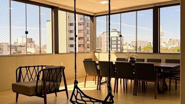 A spacious room with large windows, a hanging chair, a dining table with chairs, and a view of the cityscape.