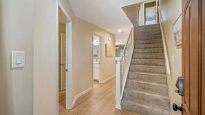 A hallway with a carpeted staircase leading to a kitchen area.