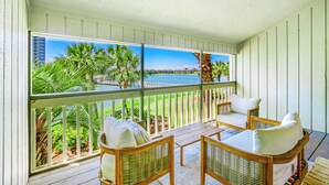 A balcony with wicker furniture and a view of the ocean and palm trees.