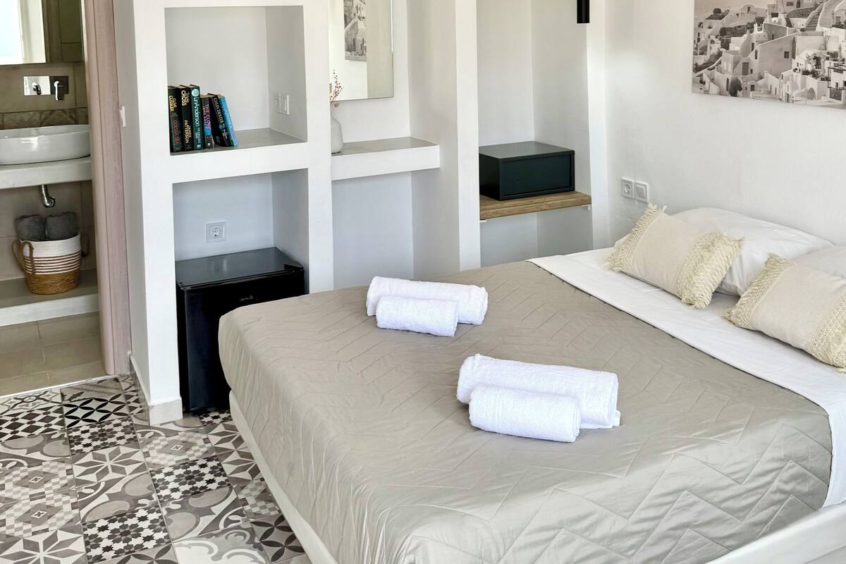 Un dormitorio moderno con cama, mesitas de noche, espejo y televisor de pared.