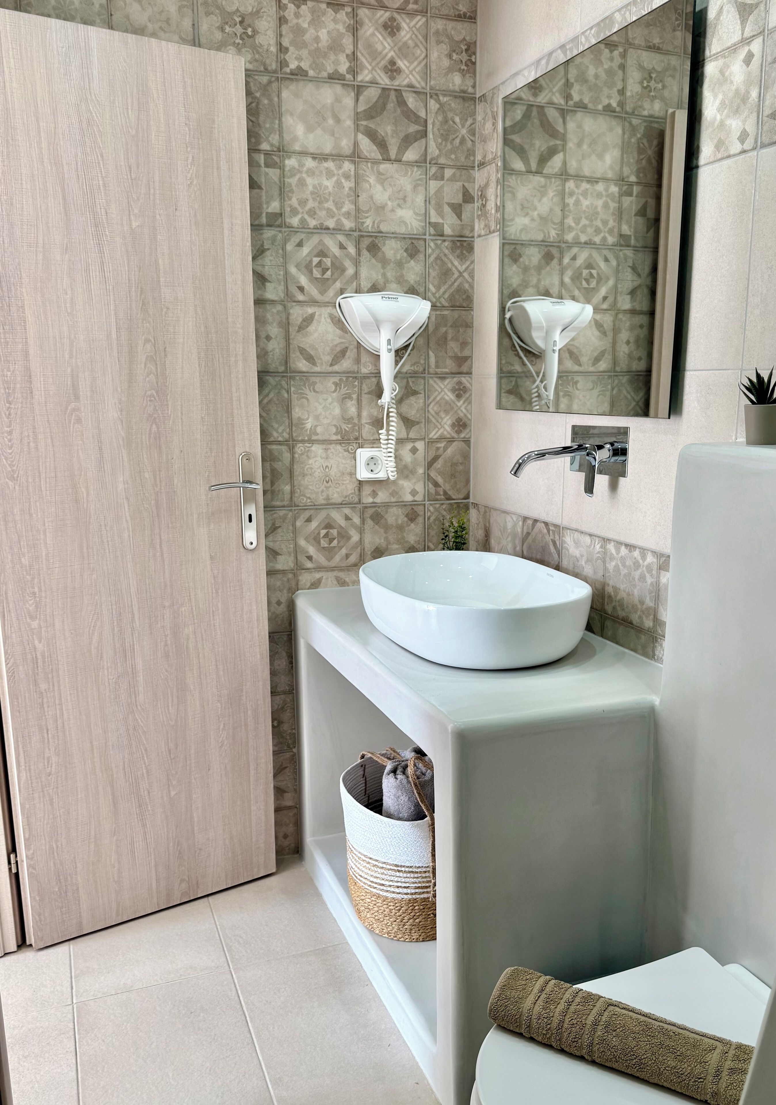 A modern bathroom with a wooden door, a white sink, a mirror, and patterned tiles.