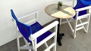 Un balcon avec deux chaises blanches et une table ronde, d’où l’on peut admirer un paysage verdoyant et une ville au loin.