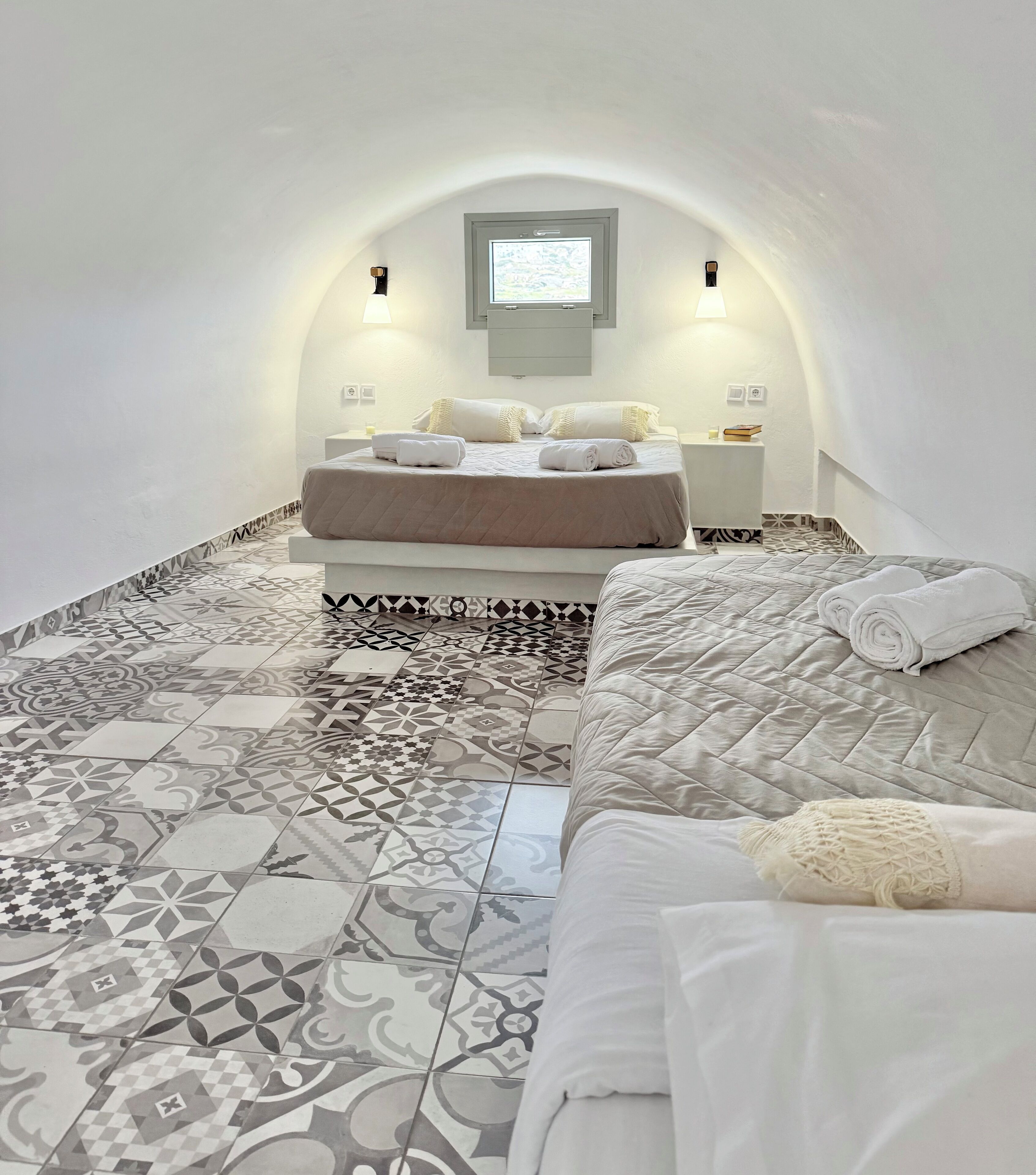 A cozy, well-lit bedroom with a large bed, a small bedside table, and a unique arched ceiling.
