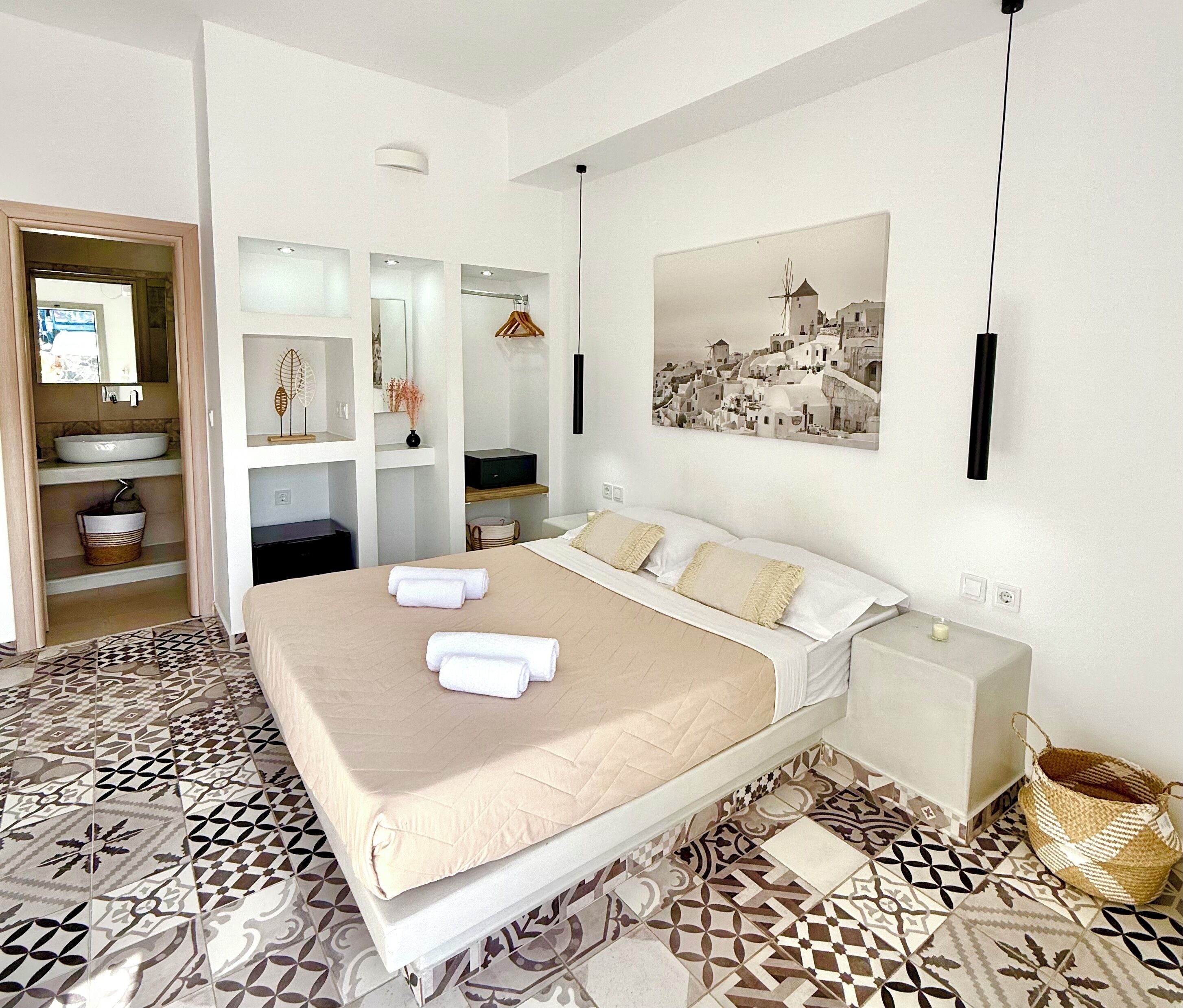 Un dormitorio moderno con una cama grande, una mesita de noche, un televisor montado en la pared y un baño con lavabo y espejo.