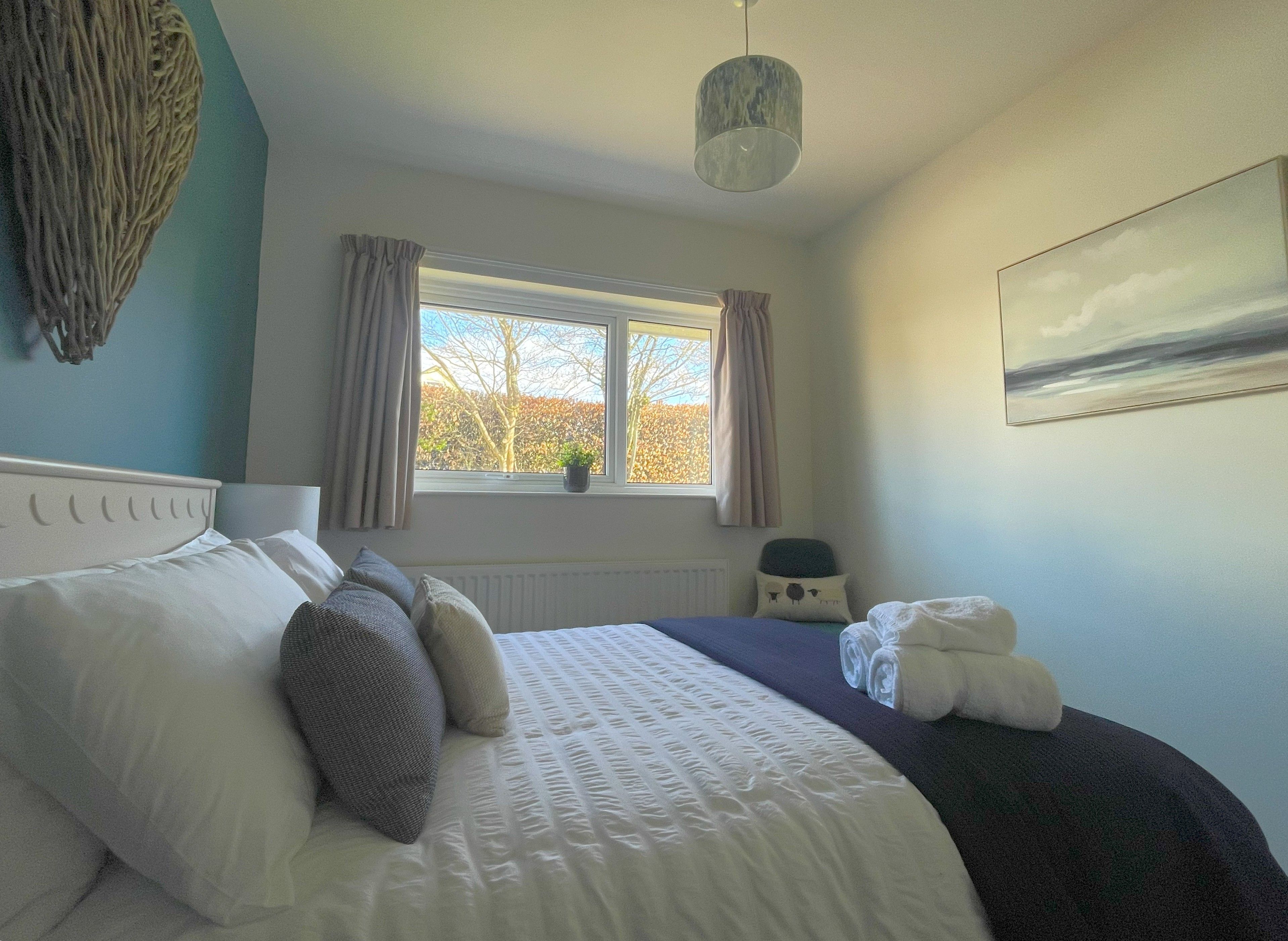 A bedroom with a bed, a window with curtains, a radiator, a hanging light fixture, and a painting on the wall.