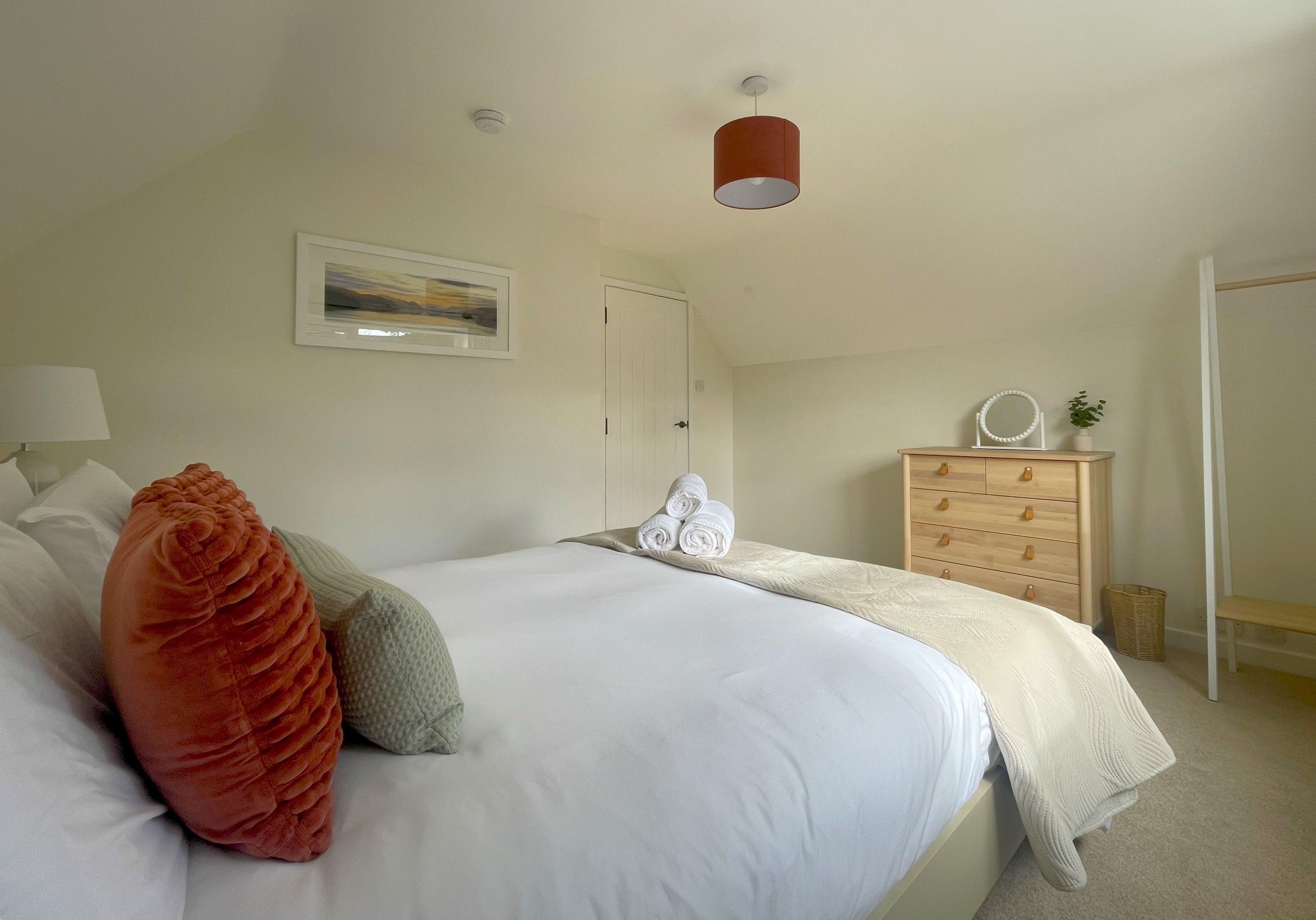 A bedroom with a bed, a wooden dresser, a mirror, and a painting on the wall.
