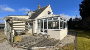 Ein Haus mit einer Holzterrasse, einem Wintergarten und einem kleinen Garten.