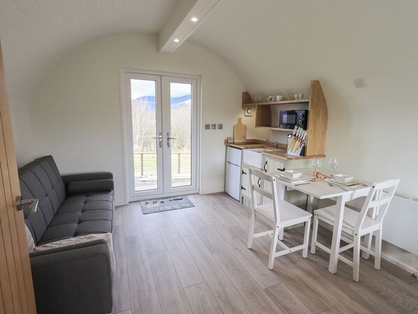 A compact living space with a sofa, dining table, chairs, a kitchen area, and a sliding glass door leading to an outdoor area.