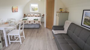 Ein gemütliches Zimmer mit einem Bett, einem grauen Sofa, einem Esstisch mit Stühlen und einer kleinen Kommode.