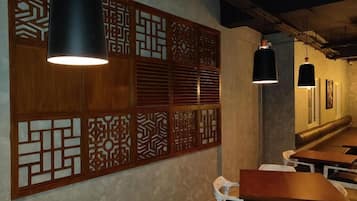 Interior de restaurante con separadores de madera, luces colgantes y sillas blancas.