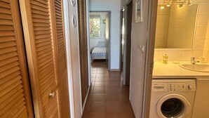 Un pasillo estrecho con puertas de madera a un lado y una lavadora al otro.
