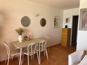 A dining area with a table, chairs, a vase with flowers, a bottle, and a basket. - New waterfront apartment for rent (Saint-Cyr-sur-Mer)