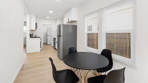 A modern kitchen with white cabinets, a grey refrigerator, and a dining area with a round table and four chairs.