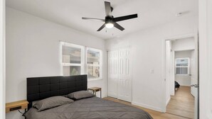 A bedroom with a bed, a ceiling fan, and a door leading to another room.
